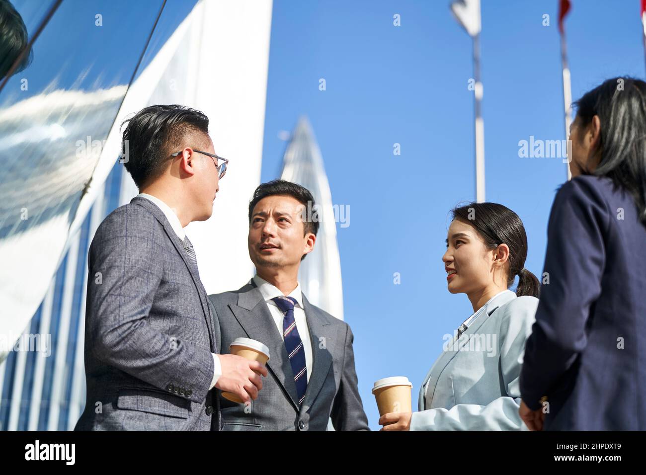 Gruppe von vier jungen asiatischen Geschäftsleuten, die draußen auf der Straße plaudern Stockfoto