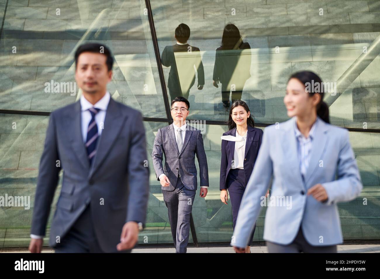 Vier junge asiatische Geschäftsleute, Männer und Frauen, die draußen gehen, konzentrieren sich auf den Hintergrund Stockfoto