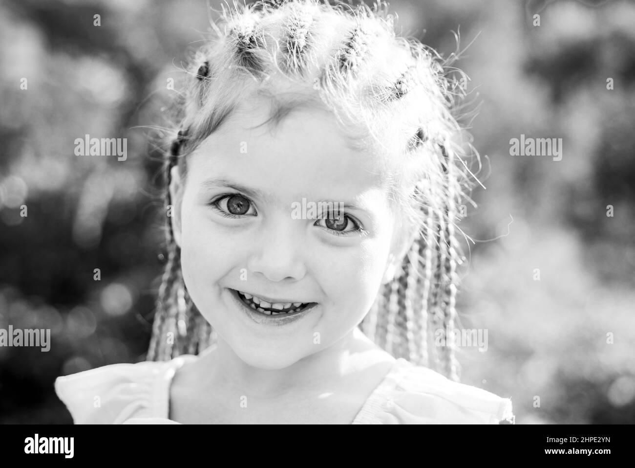 Mädchen lächelt mit Frisur Dreadlocks. Kind mit modischen Haaren im Freien. Glückliches Kind draußen. Stockfoto