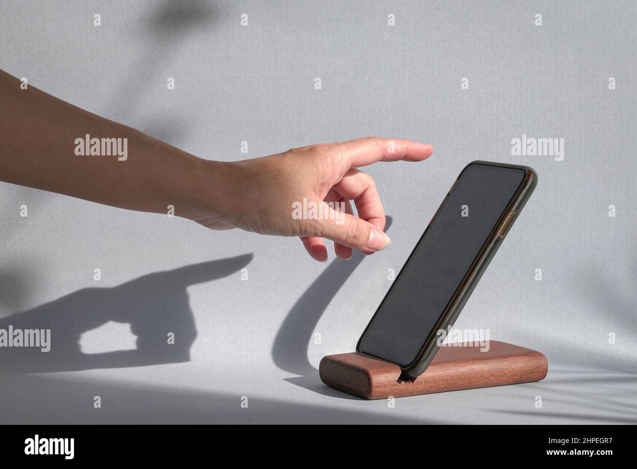 Finger, der auf ein Smartphone streut, das auf einem Halter steht, mit Schatten an der Wand. Nachbau-Remplate. Stockfoto