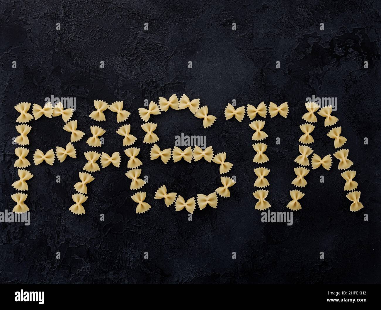 Wortpasta aus roher Farfalle (Fliege) auf dunklem Hintergrund. Stockfoto