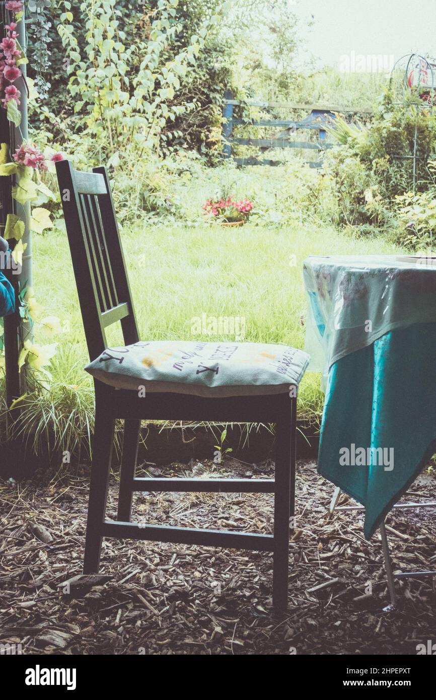 Vertikale Aufnahme eines Holzstuhls vor einem Tisch mit einem Garten im Hintergrund Stockfoto