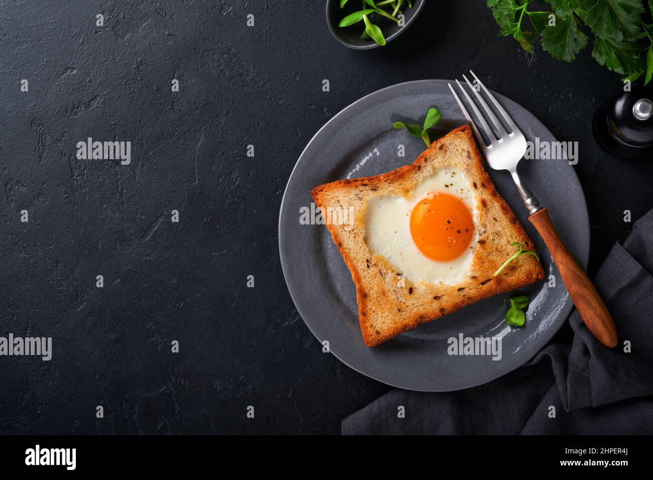 Frühstück am Valentinstag. Spiegeleier und Brot in Herzform und frisches Gemüse auf schwarzem Hintergrund. Frühstück mit Überraschung für geliebt Stockfoto