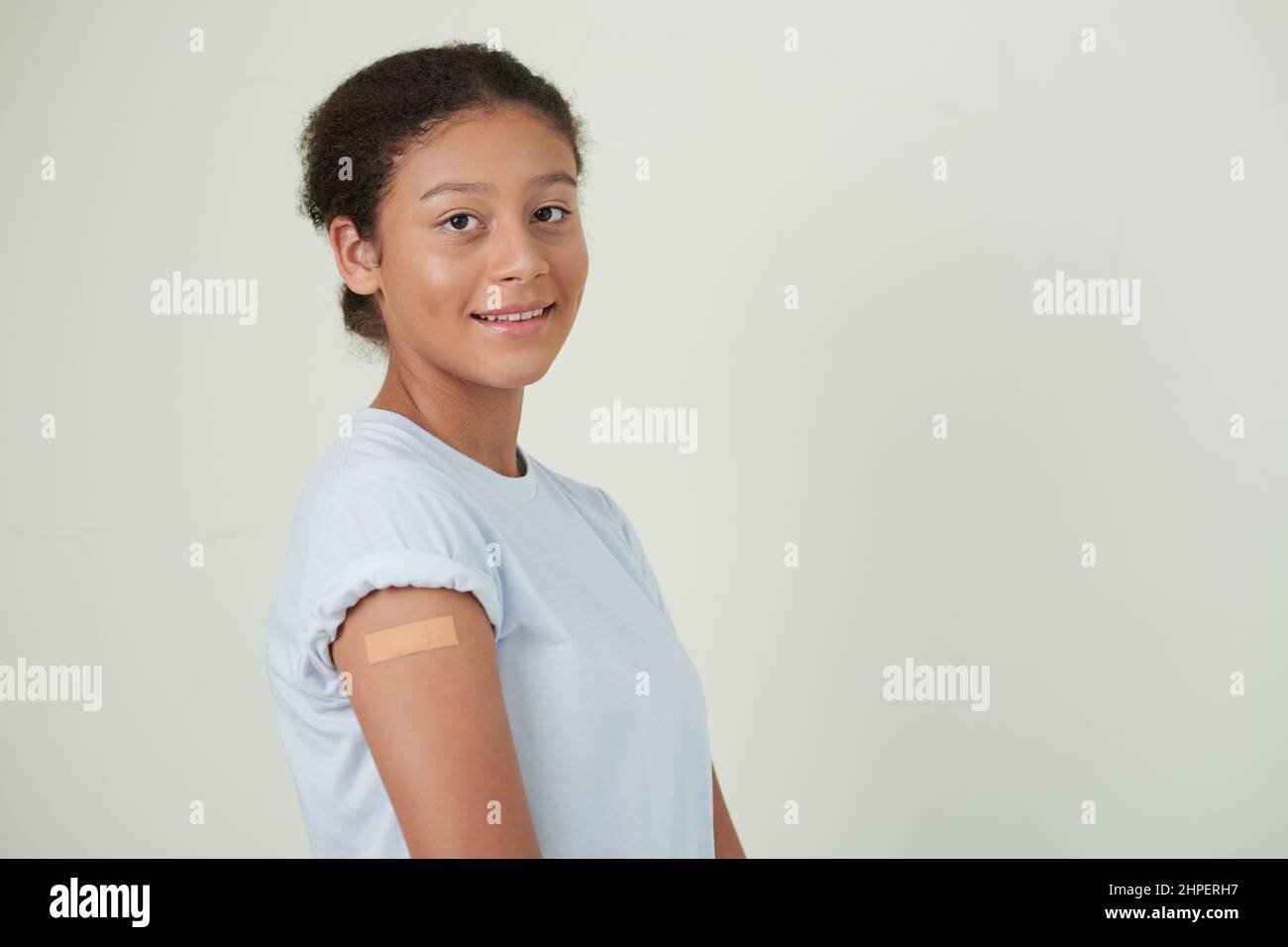 Porträt eines Teenagers mit Gips auf ihrem Arm, das vor dem weißen Hintergrund vor der Kamera lächelt und sich impfen lässt Stockfoto