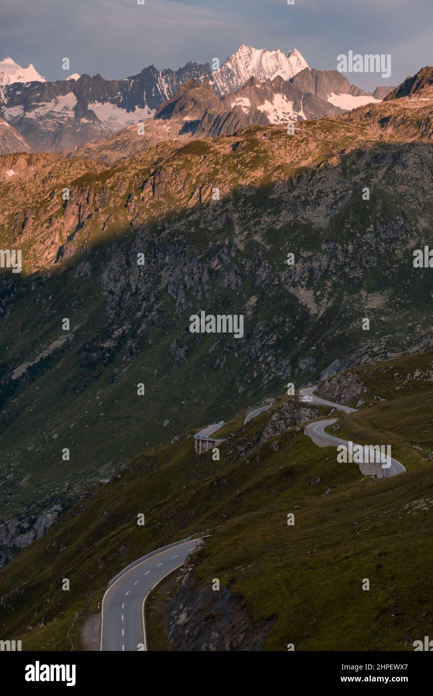 Leere asphaltierte Bergstraße schlängelt sich durch die Landschaft. Auf einer kleinen Schotterpiste am Straßenrand ist ein Wohnmobil geparkt. Die Landschaft ist felsig und mit Wiesen, ohne Bäume. Stockfoto