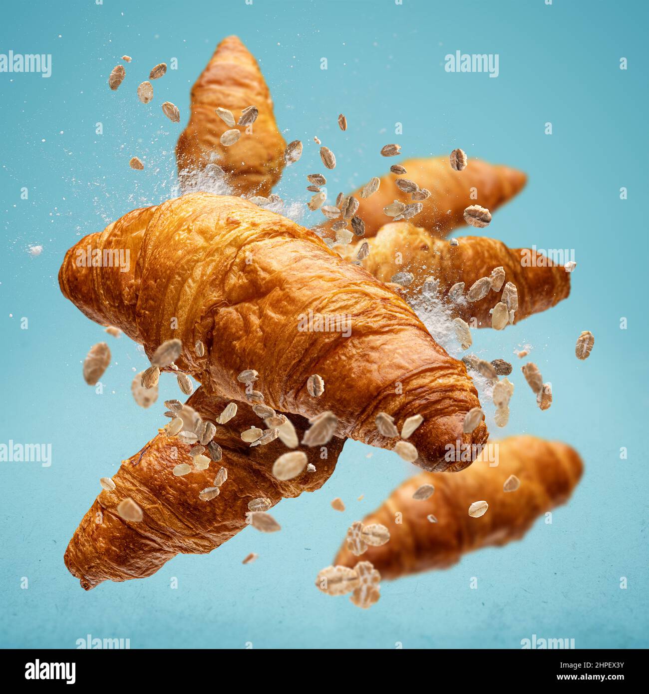 Frisch gebackene Croissants fliegen in der Luft auf blauem Hintergrund Stockfoto