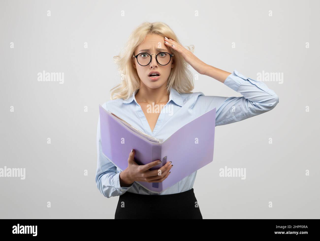 Gestresste junge Büroangestellte mit Dokumenten, schockiert über Fehler, fehlende Frist, posiert auf hellgrauem Hintergrund Stockfoto