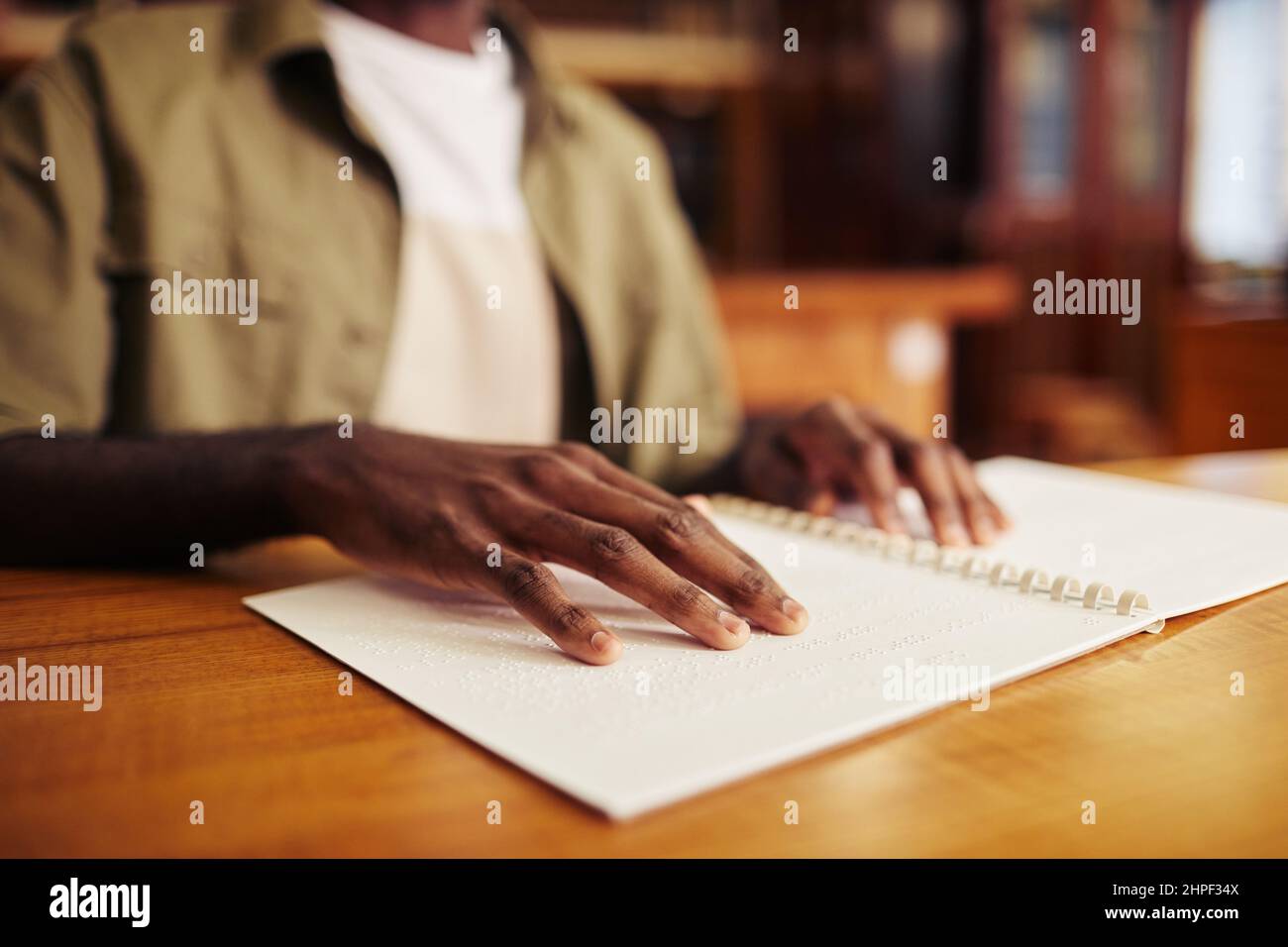 Nahaufnahme eines jungen schwarzen Mannes mit Sehbehinderung beim Lesen eines Buches in Braille am Tisch in der Universitätsbibliothek Stockfoto