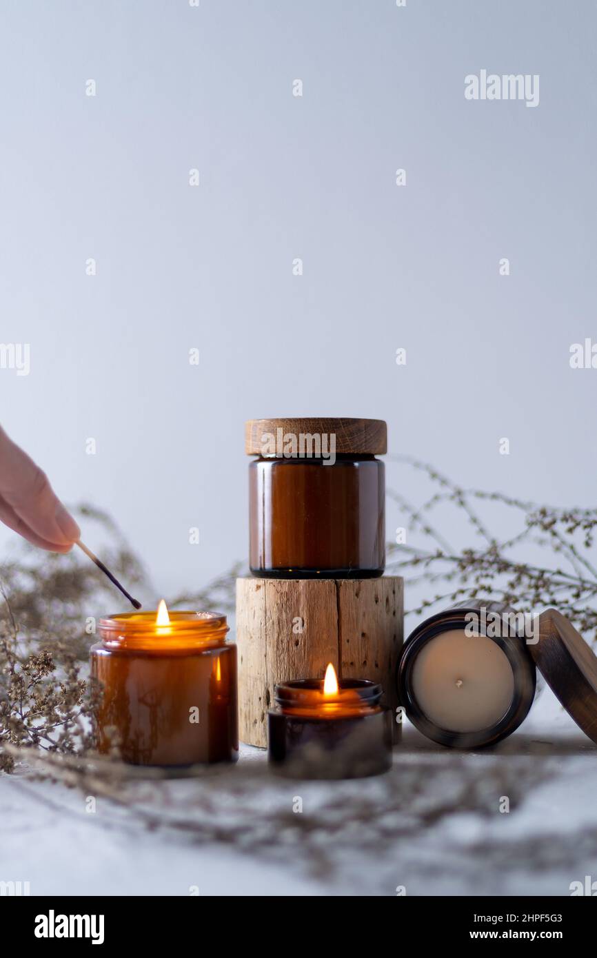 Ein Set von Sojakerzen in einem braunen Glasgefäß mit einem Holzdeckel. Brennende Duftkerze. Zünden Sie Kerzen mit einem Streichholz an. Gemütlich und gemütlich. Aromatherapie. Stockfoto