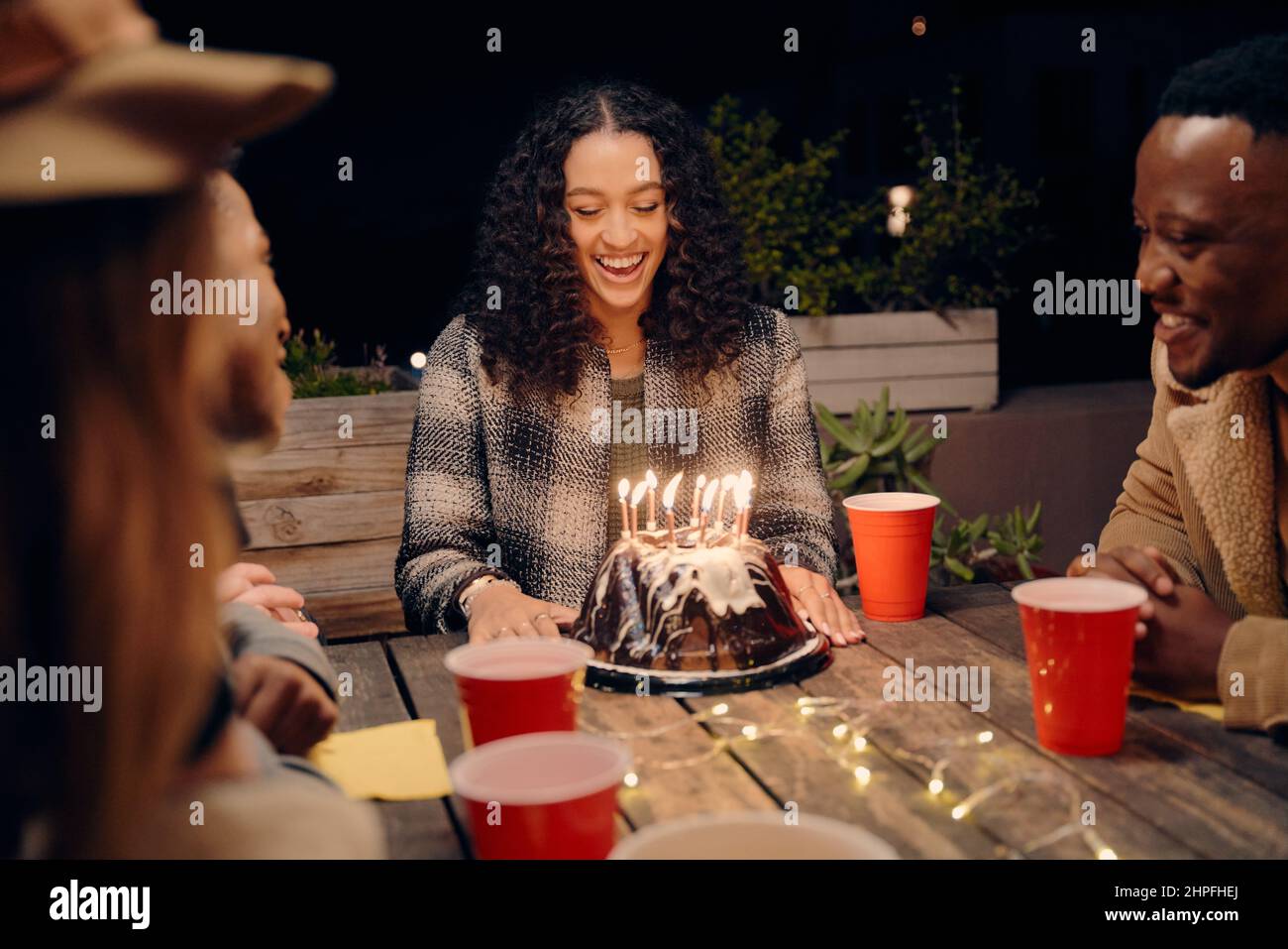 Geburtstagskind sitzt mit einer Gruppe von verschiedenen jungen Erwachsenen auf dem Dach Party Beleuchtung Wunderkerzen von Geburtstagskuchen. Stockfoto