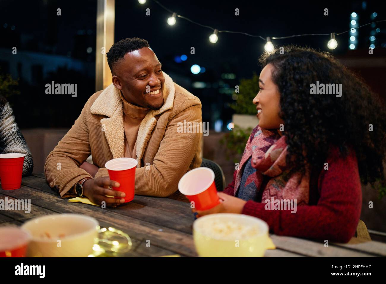 Biracial weiblich und schwarz männlich reden, während auf einer Dachparty in der Stadt. Trendy, trinken mit roten Tassen. Stockfoto