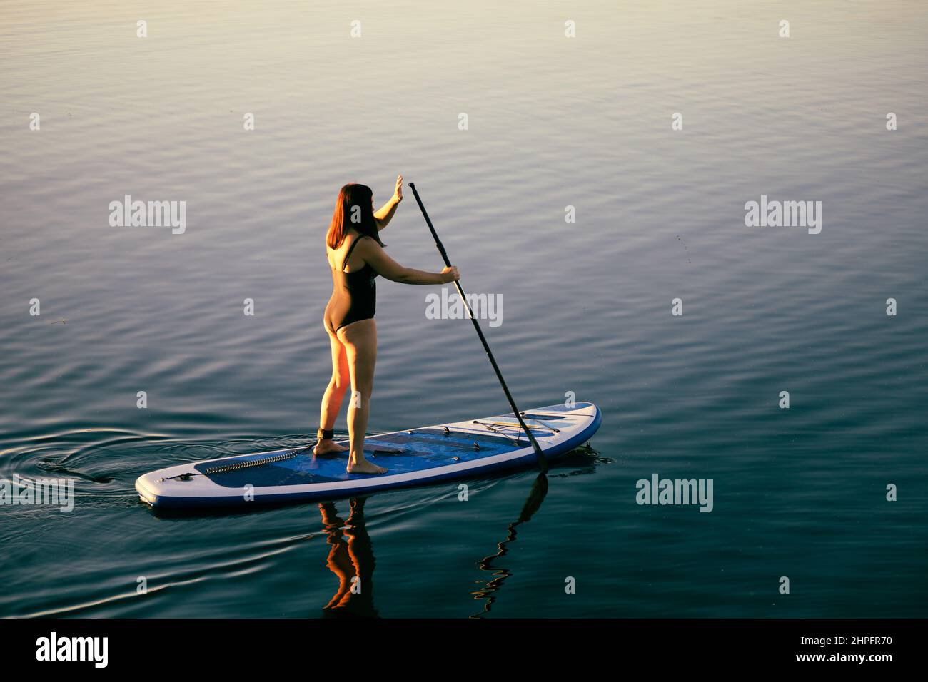 Blick von oben auf eine entspannte Frau mittleren Alters auf dem Ruderboot mit Rudern auf dem ruhigen Seewasser. Aktiver Lebensstil. Freizeitaktivitäten für Menschen von Stockfoto