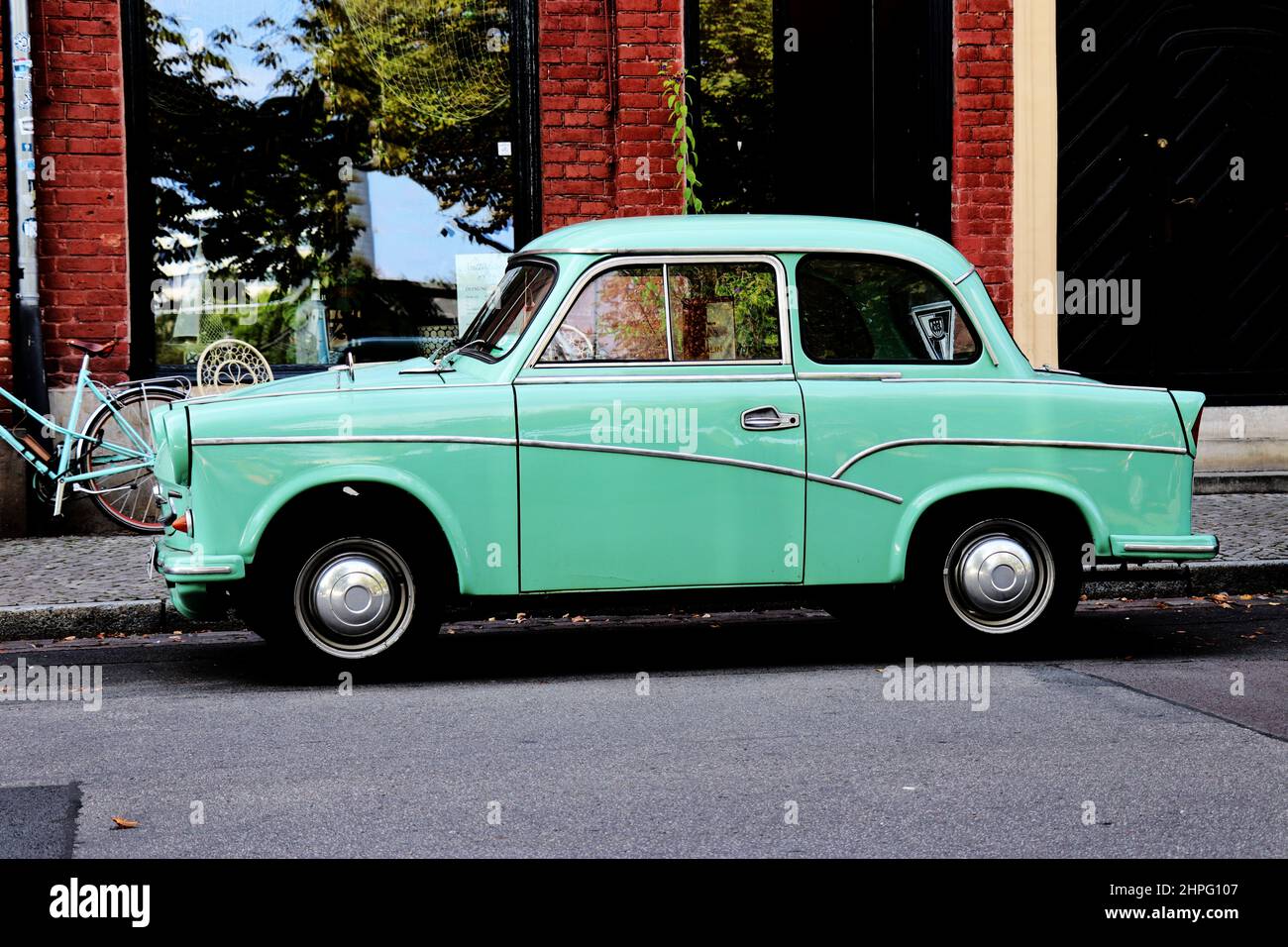 Grün - türkisfarbener trabant, umgebaut als Cadillac-Auto und türkisfarbenes Fahrrad, das vor einem Geschäft steht Stockfoto