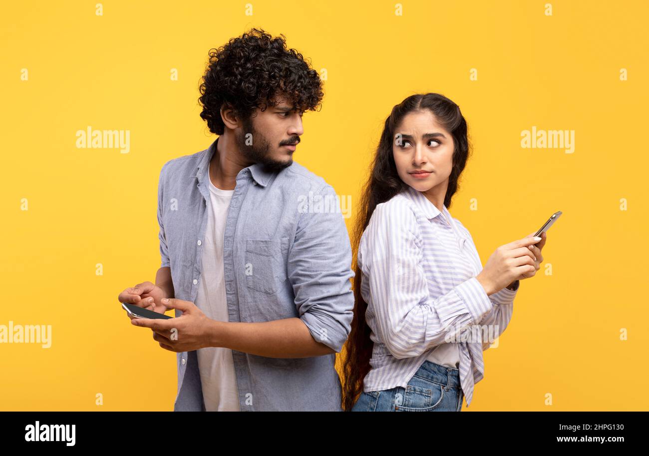 Datenschutzkonzept. Indischer Mann, der versucht, das Smartphone seiner Freundin zu betrachten, Frau, die den Bildschirm ihres Gadgets versteckt Stockfoto