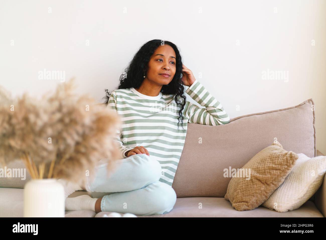 Glückliche afroamerikanische Frau, die im Wohnzimmer auf dem Sofa sitzt Stockfoto