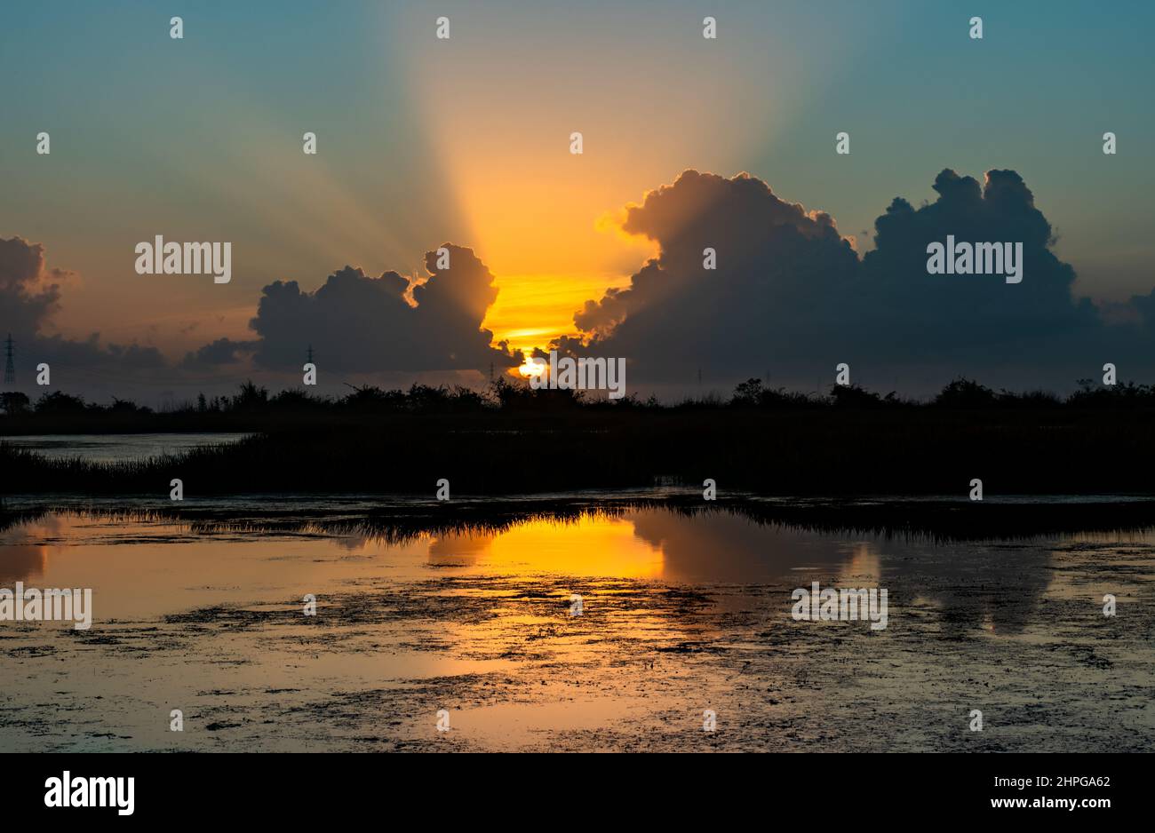 Die Sonne geht auf, Sonnenstrahlen strömen durch Wolken und spiegeln sich auf einem Teich. Stockfoto