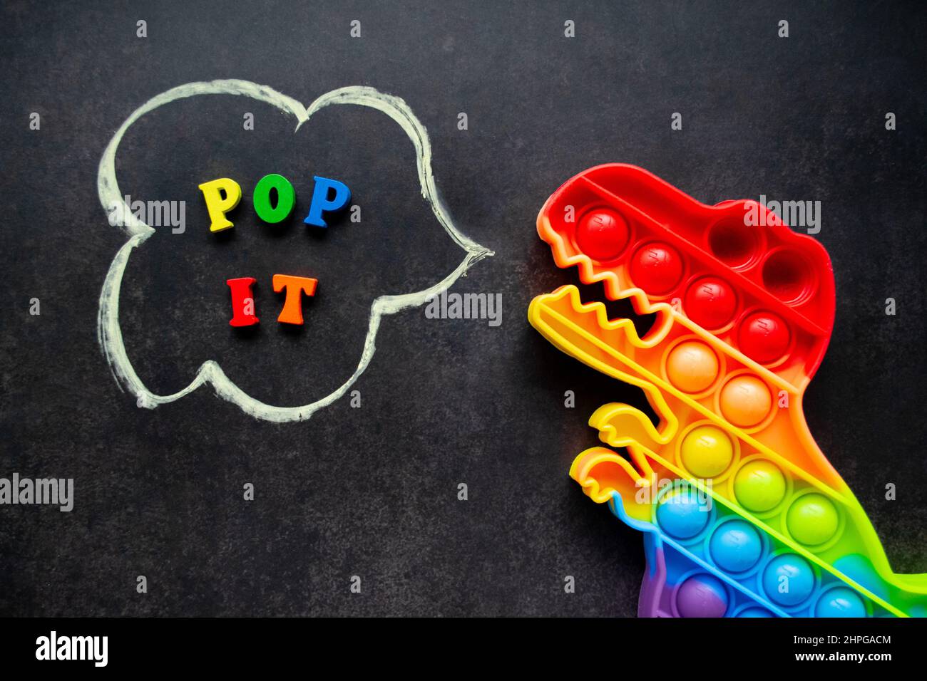 Pop it Dinosaurier Spielzeug Regenbogenfarben auf schwarzem Hintergrund mit bunten Buchstaben und der Inschrift - Pop it in einer Sprechblase. Stockfoto