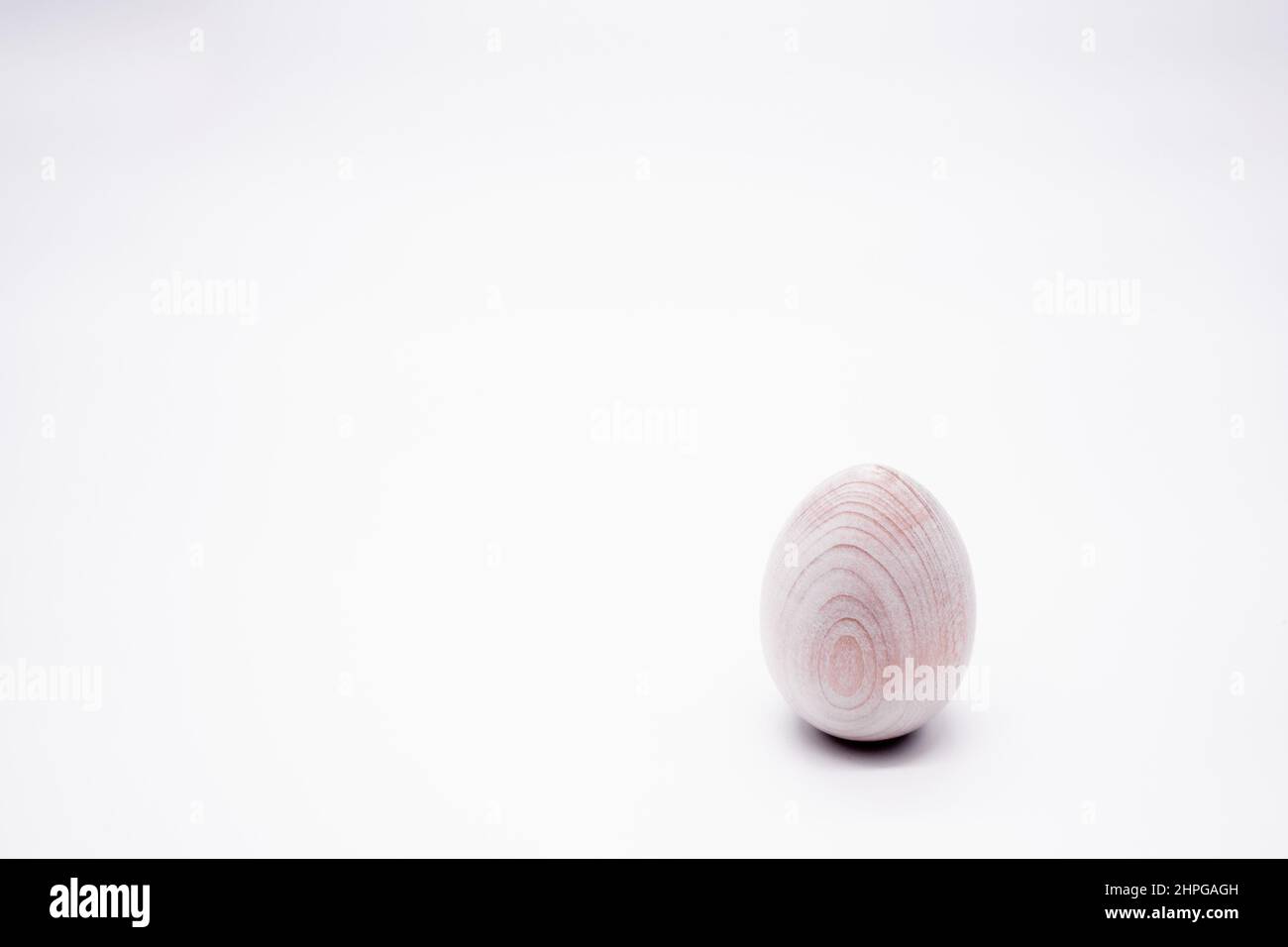 Ein unbemaltes handgemachtes Holzei auf weißem Hintergrund. Speicherplatz kopieren. Stockfoto