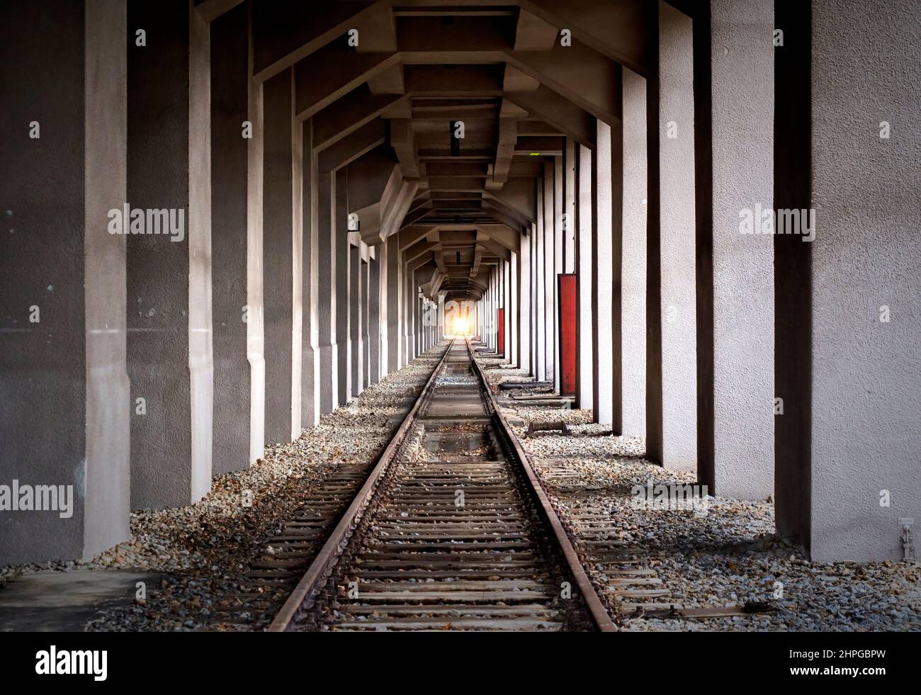 Endlose Schienen in zentraler Perspektive zwischen dicht stehenden Betonsäulen mit Licht im Fluchtpunkt, zusammengesetzt Stockfoto