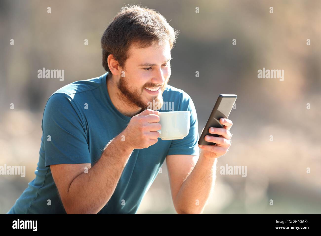 Glücklicher Mann, der mit dem Smartphone Online-Inhalte beim Kaffeetrinken im Freien beobachtet Stockfoto