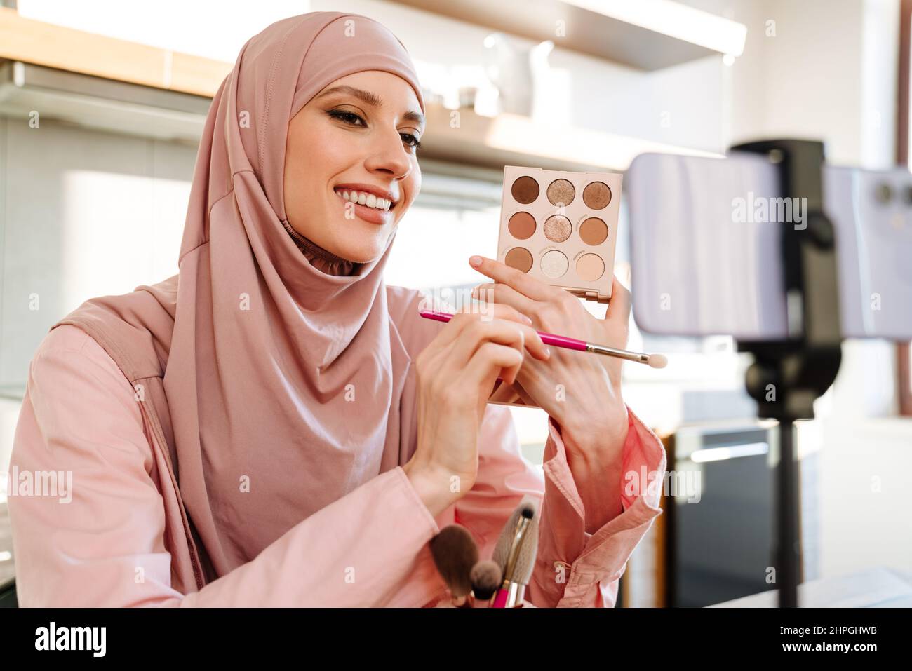 Junge muslimische Frau in Hijab vloggt sich über Beauty-Produkte mit einem Video für ihren Blog über Kosmetik mit Handy-Kamera zu Hause zu machen Stockfoto