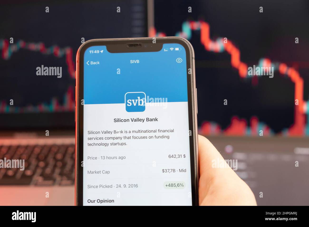 Abwärtstrend der Aktienkursen der Silicon Valley Bank mit roten Grafiken im Hintergrund. Man hands Holding a Smartphone with Logo on the screen, February 2022, San Francisco, USA. Stockfoto