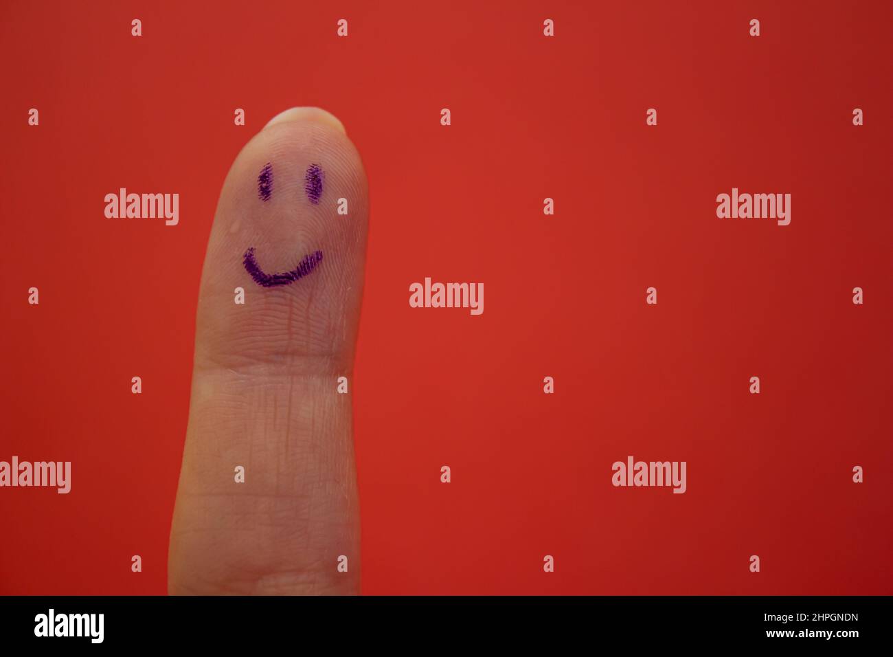 Smiley-Gesicht auf Finger isoliert auf rotem Hintergrund gezeichnet. Glücklichsein und lächelndes Konzept. Stockfoto