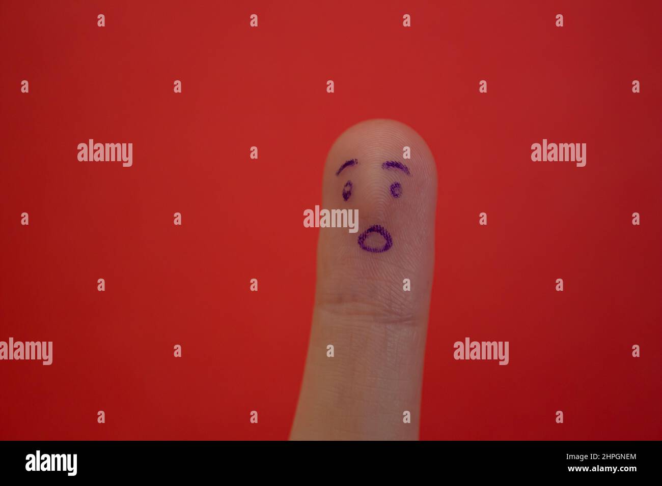 Schockiertes Gesicht auf Finger isoliert auf rotem Hintergrund gezeichnet. Witziger Gesichtsausdruck am Finger. Stockfoto