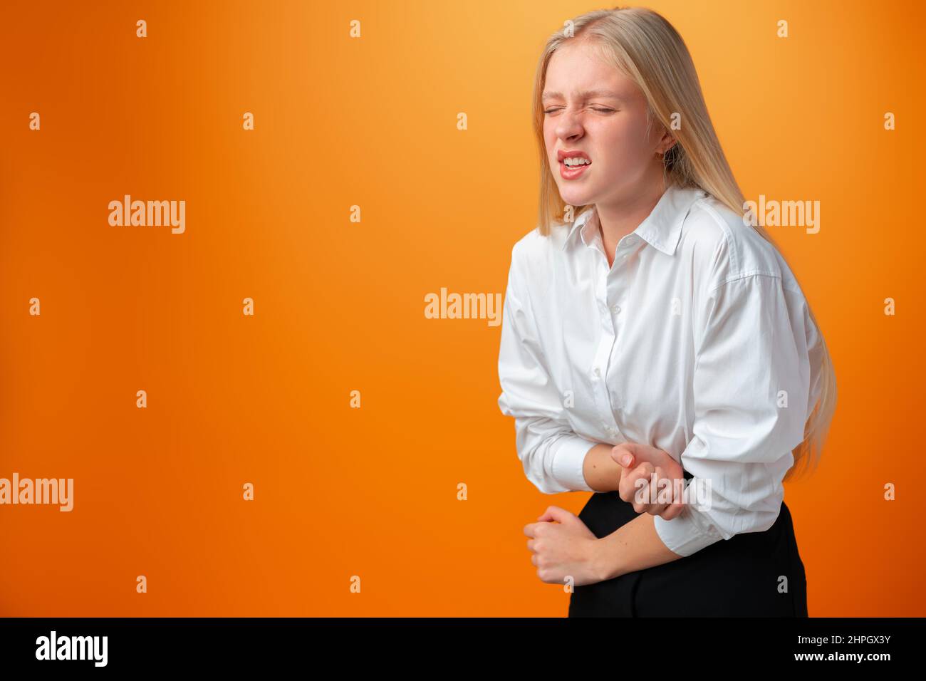 Teenager-Mädchen mit Bauchschmerzen vor orangefarbenem Hintergrund im Studio Stockfoto