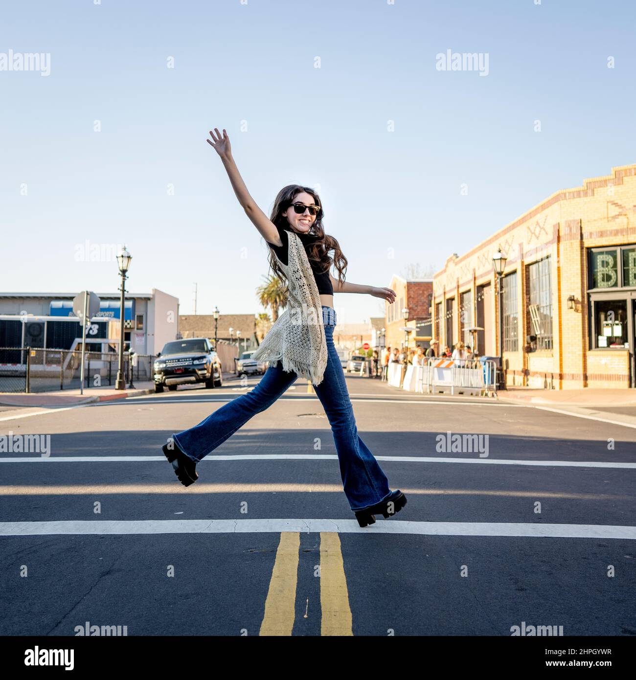 Junge Frau im Retro-Outfit von 70s überquert eine Straße in der Innenstadt Stockfoto