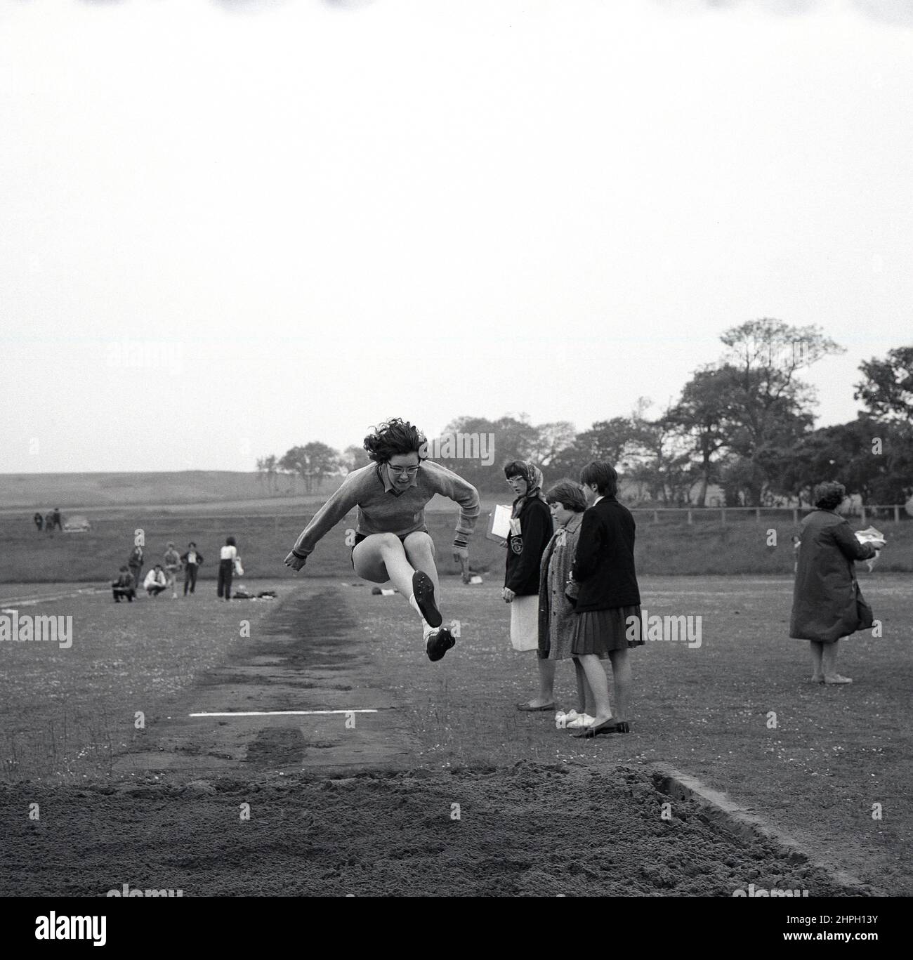 1960s, historisch, eine junge Athletin in der Luft beim Weitsprung, Fife, Schottland, Großbritannien. Geschwindigkeit, Stärke, Agilität und Entschlossenheit sind bei diesem großartigen Track-and-Field-Event gefragt, bei dem es darum geht, im Vorfeld vom Startpunkt aus so weit wie möglich in einen Sandkasten zu springen. Als Männerveranstaltung bei den ursprünglichen Olympischen Spielen von 1896 nahmen Frauen erstmals 1948 in London am olympischen Weitsprung Teil. Stockfoto