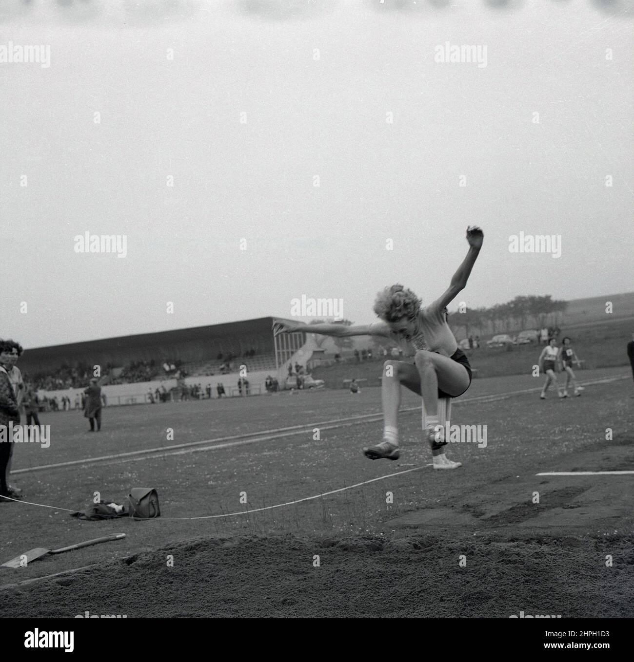 1960s, historisch, eine Athletin in der Luft beim Weitsprung, Fife, Schottland, Großbritannien. Geschwindigkeit, Stärke, Agilität und Entschlossenheit sind bei diesem großartigen Track-and-Field-Event gefragt, bei dem es darum geht, im Vorfeld vom Startpunkt aus so weit wie möglich in einen Sandkasten zu springen. Als Männerveranstaltung bei den ursprünglichen Olympischen Spielen von 1896 nahmen Frauen erstmals 1948 in London am olympischen Weitsprung Teil. Stockfoto