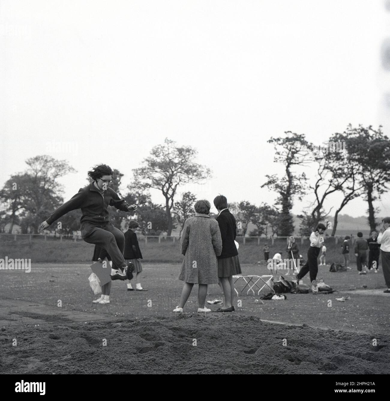 1960s, historisch, eine junge Athletin in ihrem Baumwoll-Trainingsanzug, die beim Weitsprung einen Übungs- oder Warm-up-Sprung macht, ein Leichtathletik-Event bei einem sportlichen Wettkampf, Fife, Scotand, Großbritannien. Geschwindigkeit, Kraft und Agilität sind im Weitsprung gefragt, bei dem es darum geht, im Vorfeld möglichst weit von einem Startpunkt zu springen. Bei den ersten Olympischen Spielen der Moderne 1896 nahmen Frauen erstmals 1948 am olympischen Weitsprung in London Teil. Stockfoto