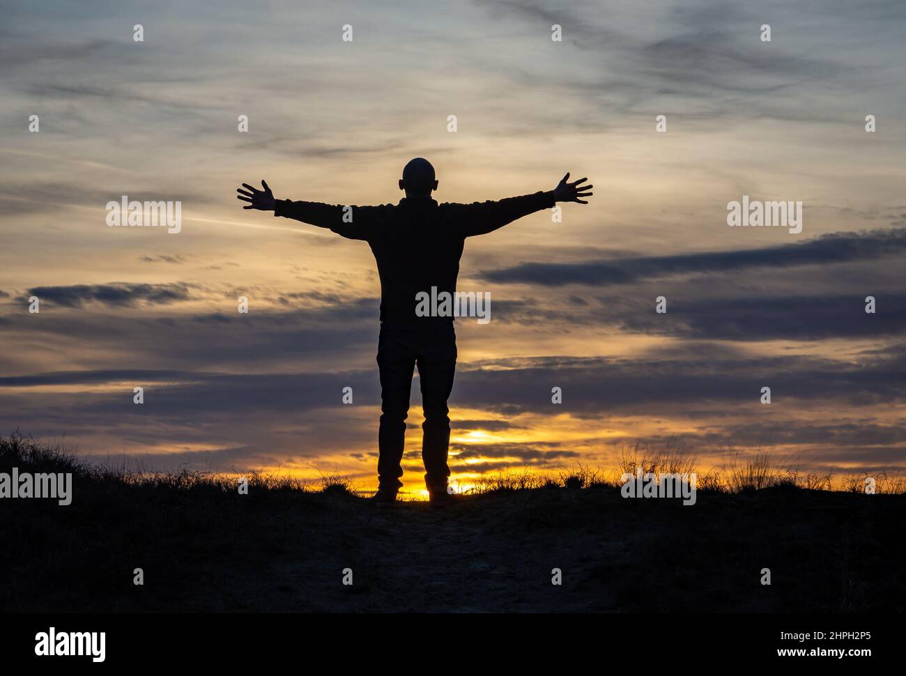 Silhouette eines Mannes, der mit ausgestreckten Händen gegen den romantischen Sonnenuntergangshimmel steht, Konzept von Freude und Glück Stockfoto