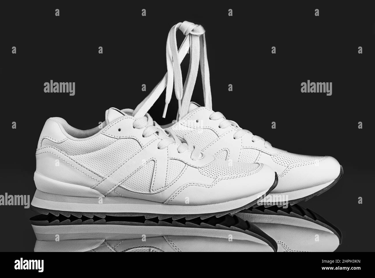 Ein Schwarz-Weiß-Foto eines athletischen Schuhepaars auf einer reflektierenden Oberfläche und einem dunklen, gradienten Hintergrund. Die erhöhten Schnürsenkel sind zu einem Schno gebunden Stockfoto