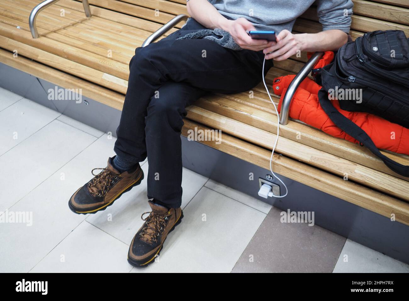 . Ein junger Mann lädt im Wartezimmer des Bahnhofs ein Mobiltelefon. Hochwertige Fotos Stockfoto