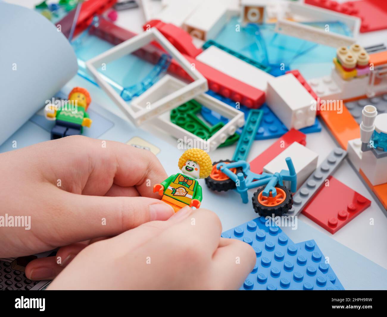 Tambow, Russische Föderation - 09. Februar 2022 Ein Kind, das eine lego Clown Minifigur in der Hand hält, während es ein Lego-Set baut. Nahaufnahme. Stockfoto