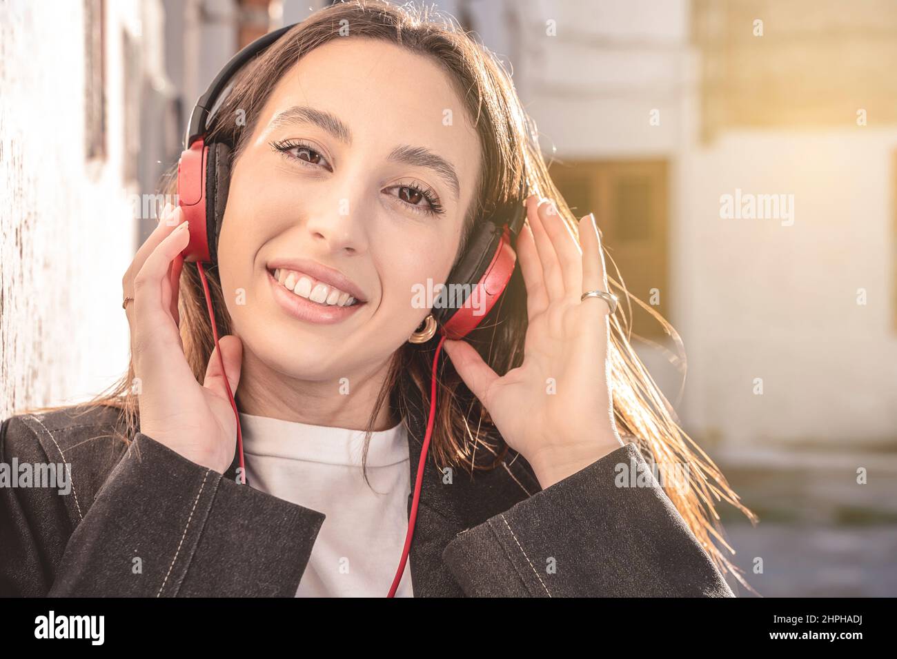 Porträt einer Millennial-Frau, die Musik in Kopfhörern genießt – lächelnd in der Stadt unterwegs Stockfoto