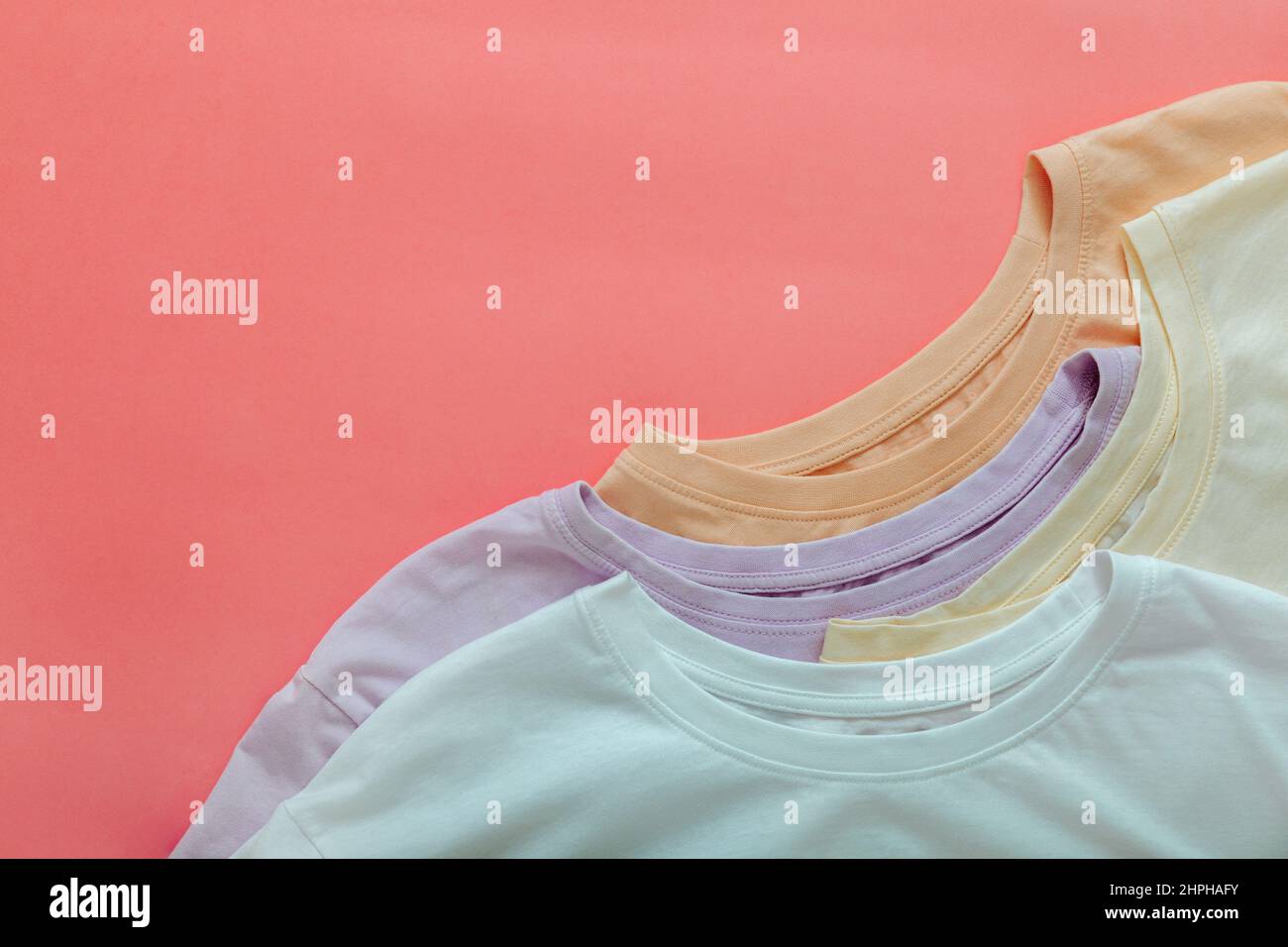 Mehrfarbige T-Shirts Pastellfarben Beige Weiß Lila.T-Shirts Mockup für Design auf Farbe Koralle rosa Hintergrund. Gestapelte Basic T-Shirts Stockfoto
