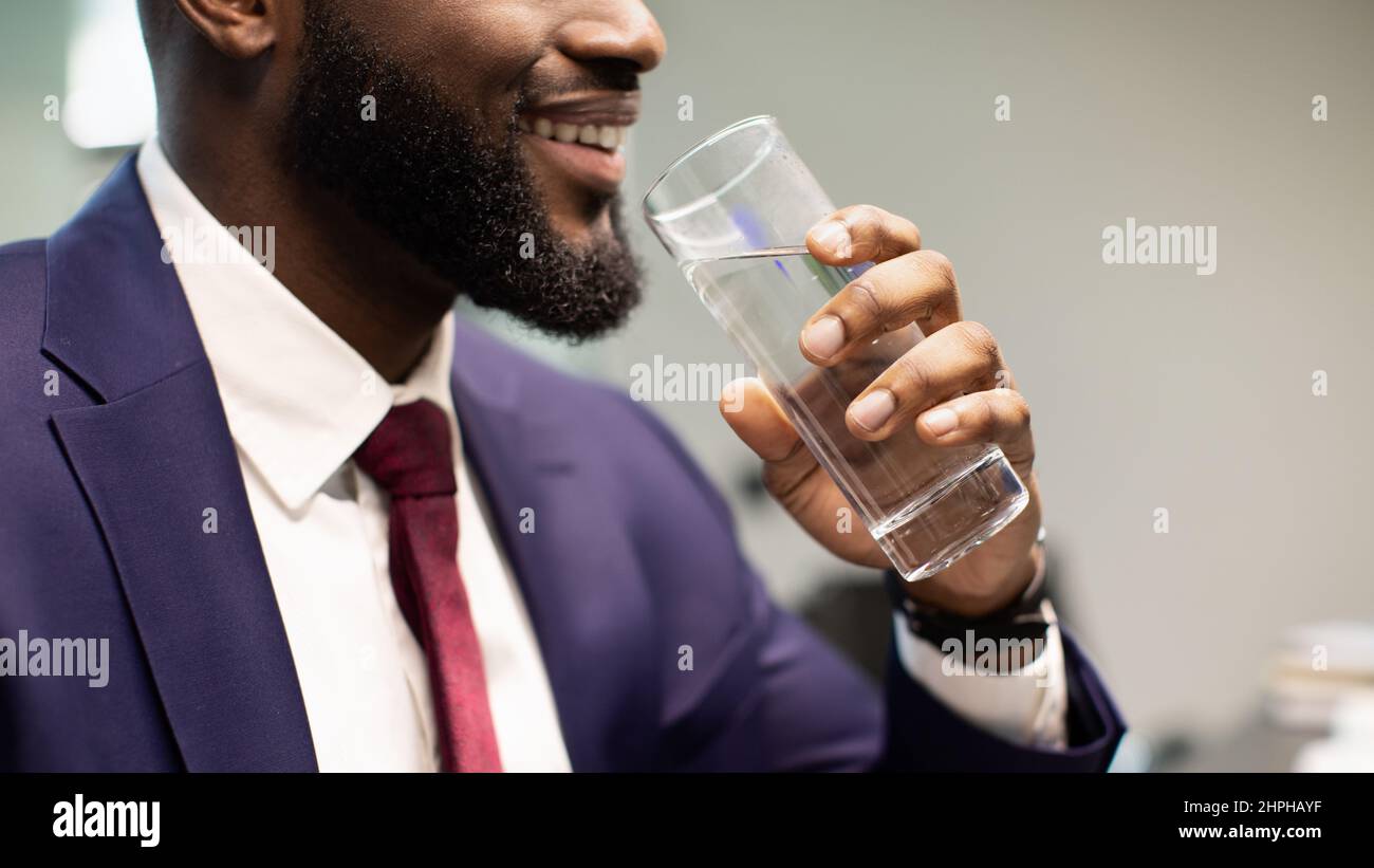 Nicht erkennbarer bärtiger schwarzer Mann im Anzug mit Trinkwasser Stockfoto