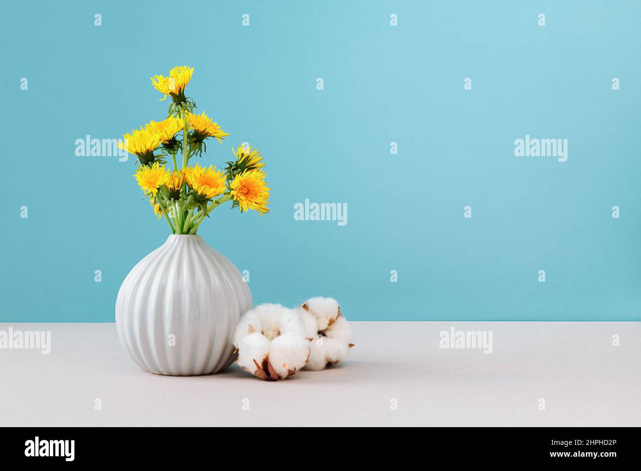 Gelbe Delelionen in Vase auf cyanfarbenem Hintergrund, Nahaufnahme, Kopierraum. Blumenstrauß sonnige Wildblumen-Elendelionen in Keramikvase in hellem Hintergrund. Stockfoto