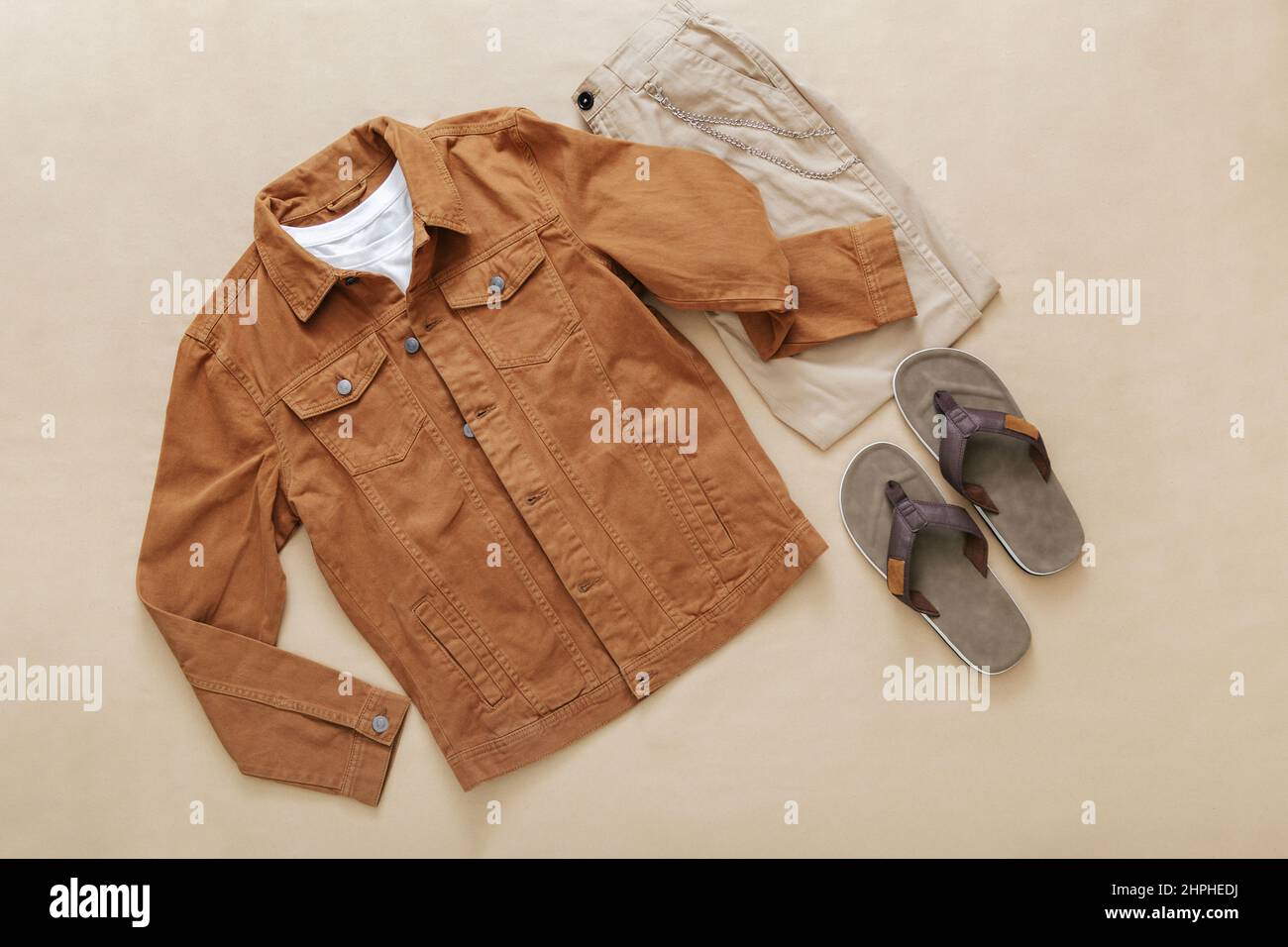 Set von stilvollen Kleidung Flip Flop Schiefer T-Shirt Hose Denim Jacke auf beigem Hintergrund Draufsicht. Sommerkleidung für Herren legere Outfits. Modisch Stockfoto