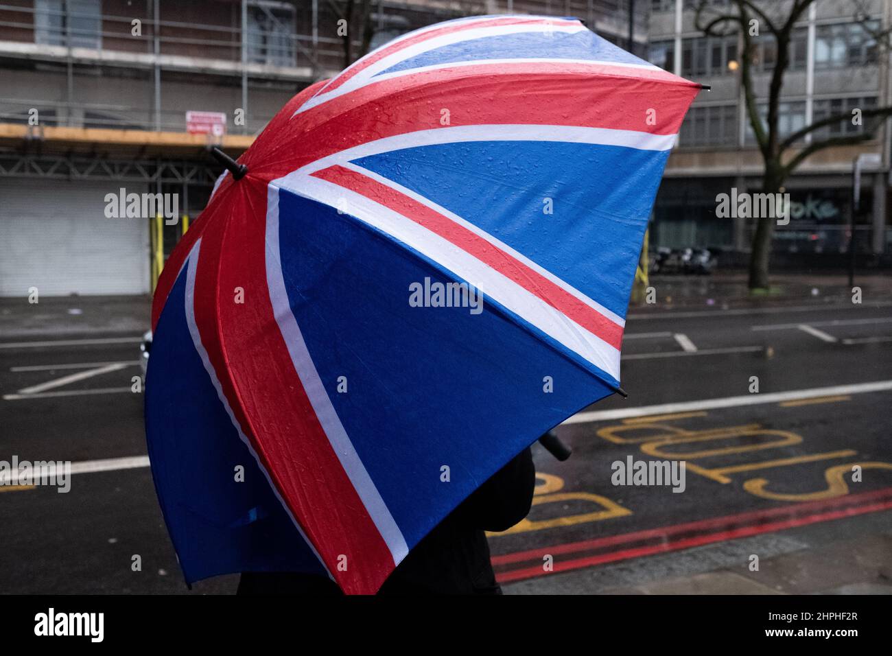 Eine Person wartet an einer Londoner Bushaltestelle mit einem Schirm der Union Flag Stockfoto