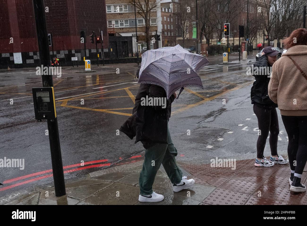 Frau, die während des stürmischen Wetters in London, Großbritannien, mit ihrem Regenschirm kämpft Stockfoto