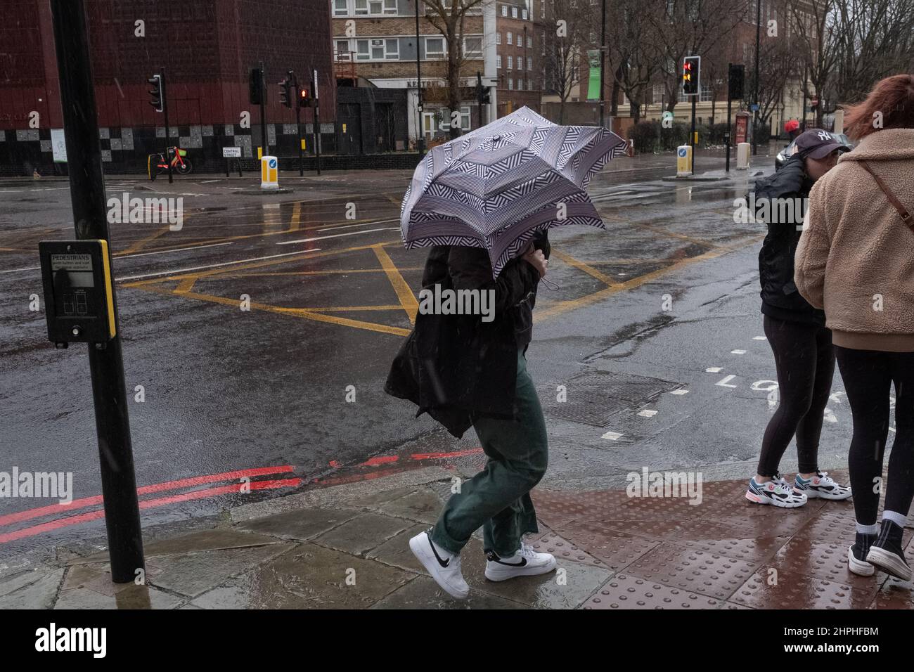 Frau, die während des stürmischen Wetters in London, Großbritannien, mit ihrem Regenschirm kämpft Stockfoto