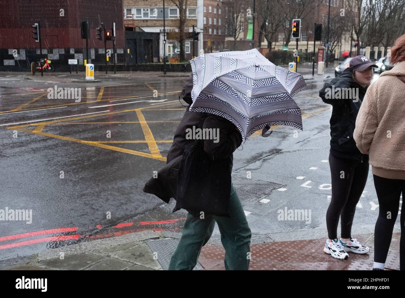 Frau, die während des stürmischen Wetters in London, Großbritannien, mit ihrem Regenschirm kämpft Stockfoto