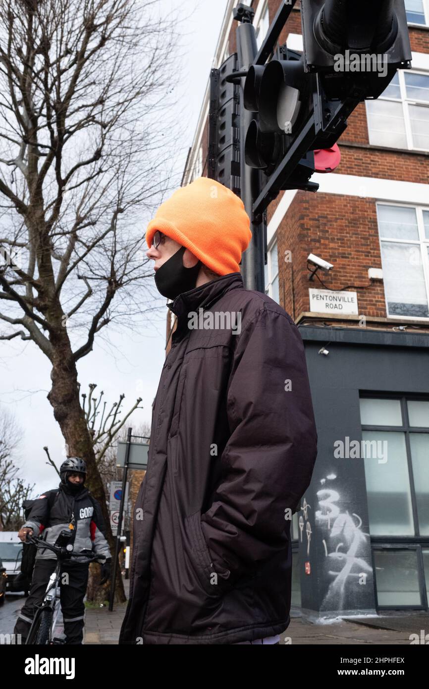 Ein Mann in einem orangefarbenen Wollhut wartet geduldig darauf, die Straße in der Nähe von Kings Cross, London, Großbritannien, zu überqueren Stockfoto