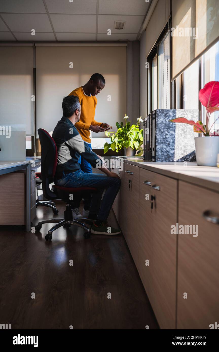 Schwarzer Mann, der seinem Partner in einem Büro eine Akte von seinem Telefon zeigt. Stockfoto