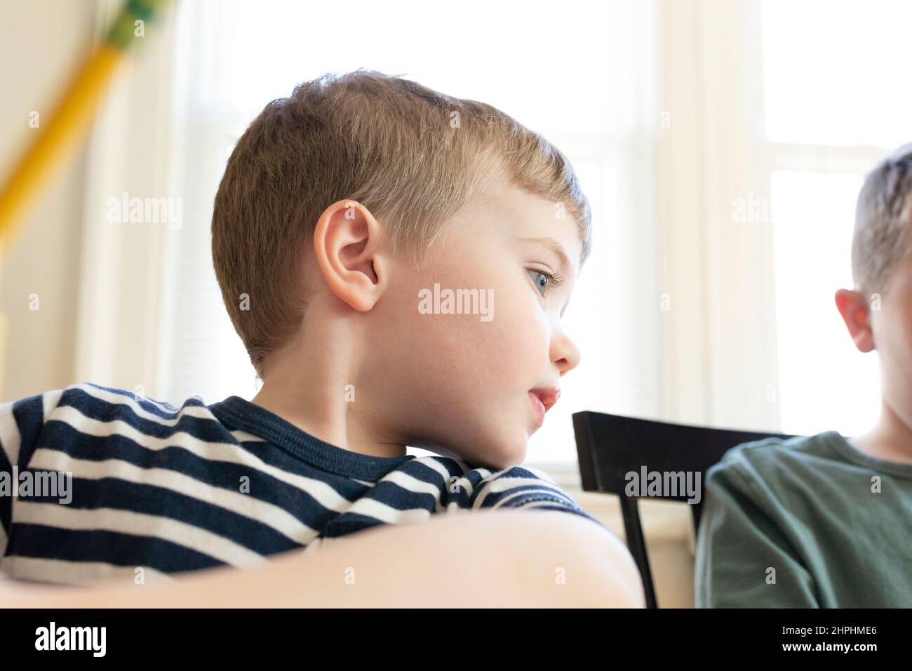 Mittlerer Schuss eines jungen Jungen, der über die Schulter schaut, während er den Bleistift hält Stockfoto