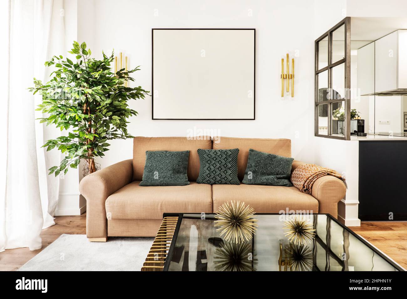 Wohnzimmer mit Glastisch, Zweisitzer-Sofa mit blauen Kissen und Kunstpflanze Stockfoto